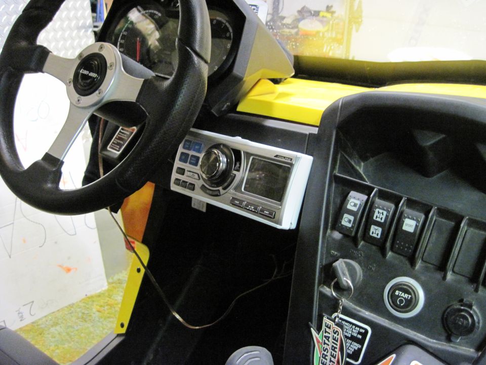 Interior of a Can-Am side-by-side with steering wheel, dashboard, and audio system visible