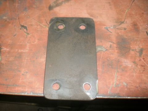 1995 Ford Bronco - A single flat steel mounting plate with rounded corners and four drilled bolt holes rests on a rust-colored metal workbench. The bare plate…