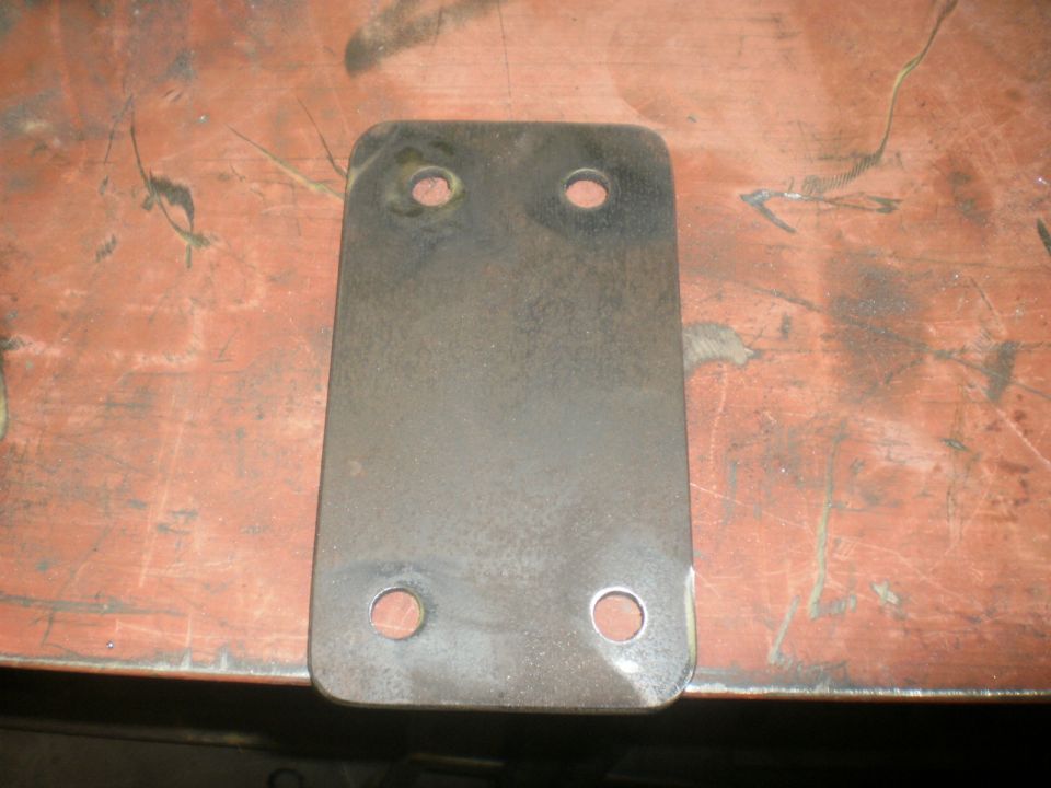 Flat fabricated steel mounting plate with four bolt holes on a workbench