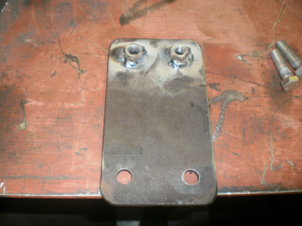 Steel bracket with welded captive nuts and two loose bolts on a workbench