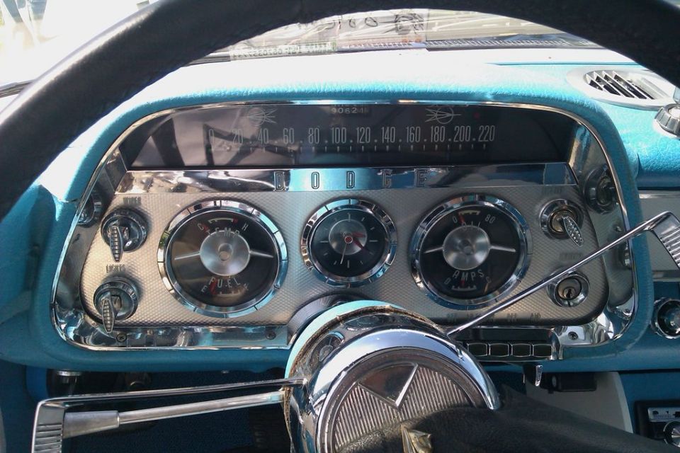 Car dashboard with round gauges, speedometer, and steering wheel. Blue interior trim