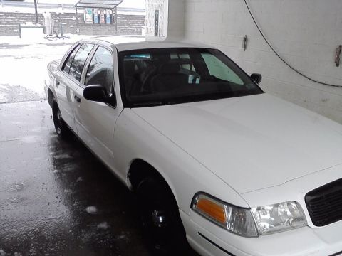 1999 Ford Crown Victoria - This white sedan, likely from the early 2000s, is shown from a three-quarter front angle in an indoor setting.