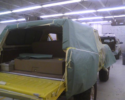1978 Ford Bronco - A 1978 Ford Bronco is covered in a green tarp in a workshop, with another vehicle visible behind it.