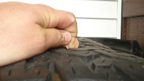 1988 Ford Bronco - A hand inserts a penny into a tire's tread to gauge its remaining depth.