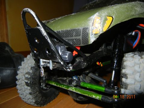 1996 Ford Bronco - Close-up of an RC car's front bumper and suspension system, showing off-road tires and green-painted suspension arms.