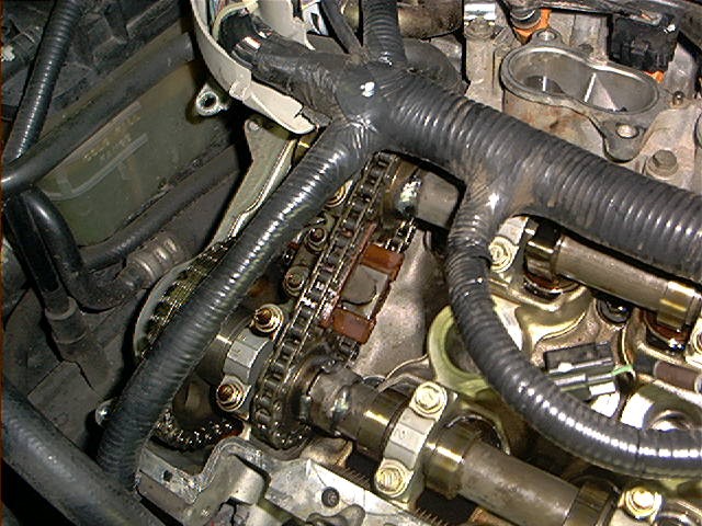 Engine timing chains and camshaft journals exposed during overhead-cam engine teardown with loomed wiring nearby