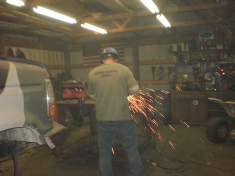 1995 Ford Bronco - A person works on a vehicle in a cluttered garage, with an American flag visible in the background.