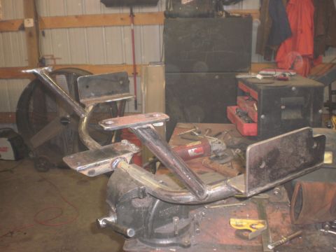 1995 Ford Bronco - A metal frame part, possibly a transmission crossmember, is secured in a vise for work. Tools and shop equipment are visible in the backgro…