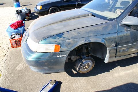1995 Ford Taurus - A green 1996 Ford Taurus is partially visible with its front passenger wheel off, revealing the brake system.