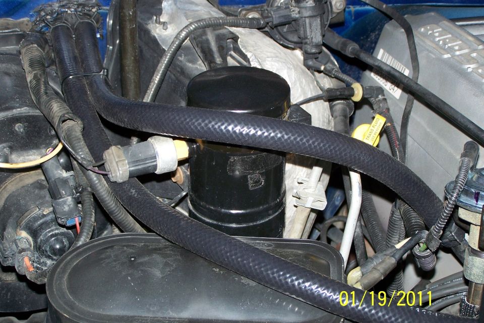 Engine bay close-up with black canister, braided hoses and wiring harnesses