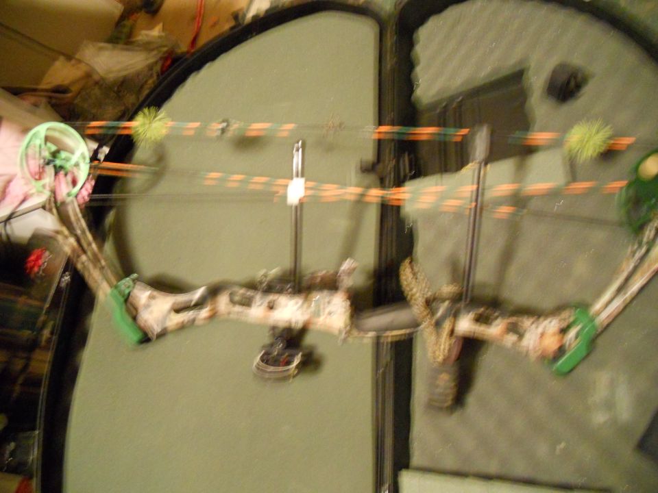 Compound bow with camouflage riser and orange/green string, inside a case
