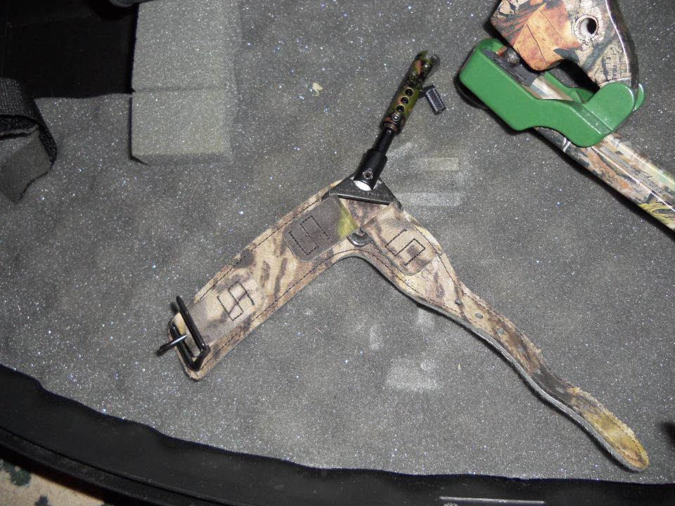 Camouflage bow sling with metal buckle and part of a compound bow with green riser, resting on foam padding