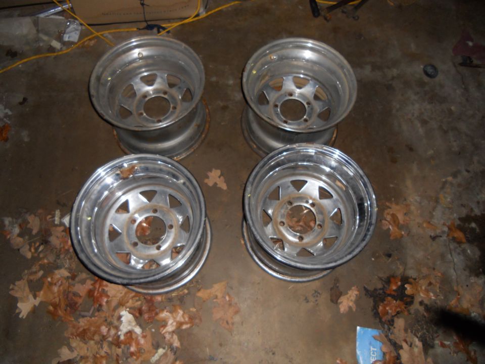 Four aluminum alloy wheels with a five-spoke design, stacked on a concrete floor