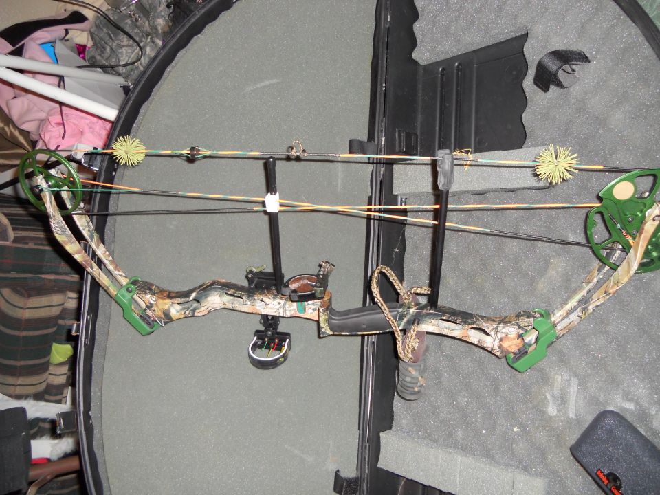 Compound bow with camouflage limbs and green accents, resting in a black case