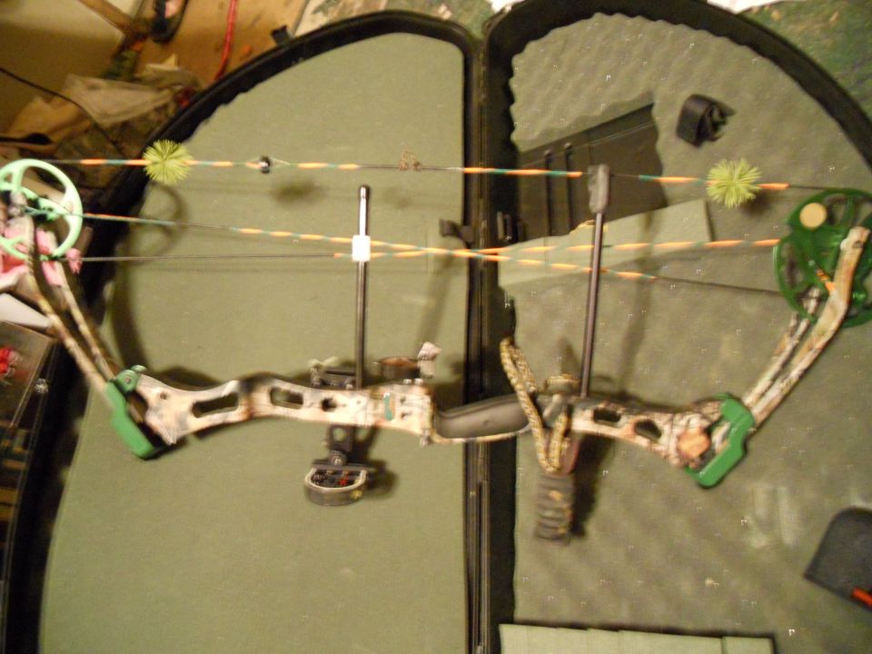 Compound bow with green accents and camouflage pattern, resting in an open case