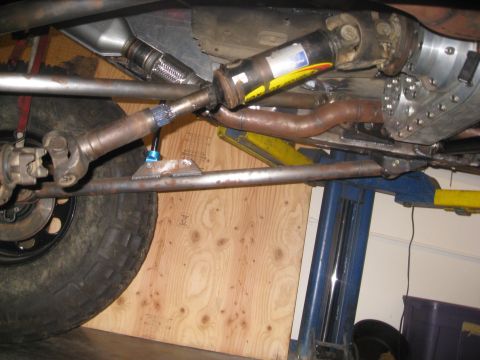 1994 Jeep YJ - Close-up view of the drive shaft and exhaust components underneath a vehicle, possibly undergoing modifications.