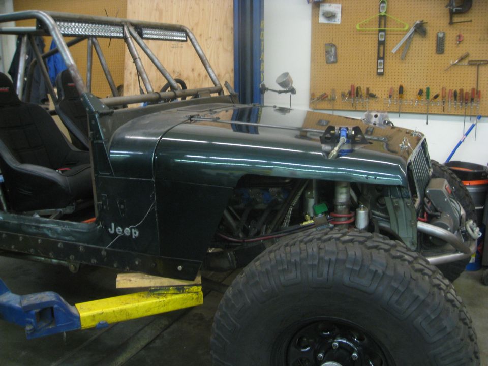 Green 1994 Jeep YJ with custom roll cage and off-road tires in a workshop