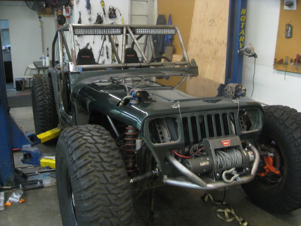 Green Jeep Wrangler with roll cage, large tires, and winch, in a garage
