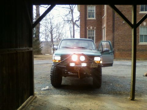 1996 Ford Bronco - A modified green Ford Bronco is parked outside a brick building with its driver's side door ajar.