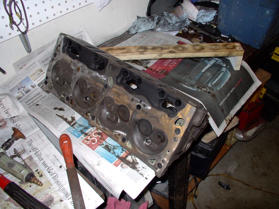 Removed cast-iron V8 cylinder head resting on newspaper on a cluttered garage workbench