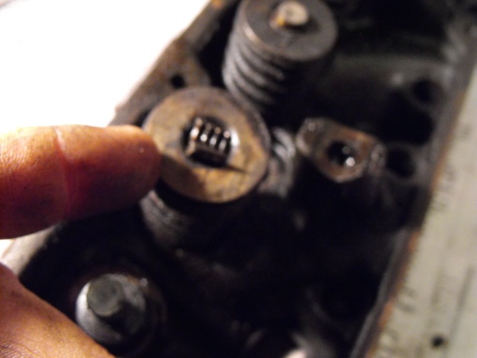 Finger pointing at valve spring retainer and keeper on a dirty engine cylinder head