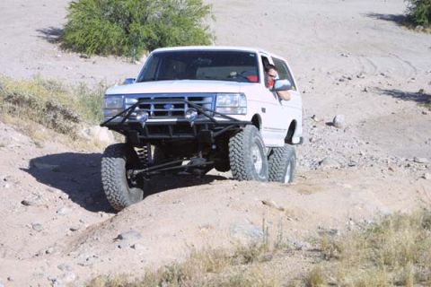 1993 Ford Bronco - A white Ford Bronco navigates a rocky, off-road trail with a driver visible inside.
