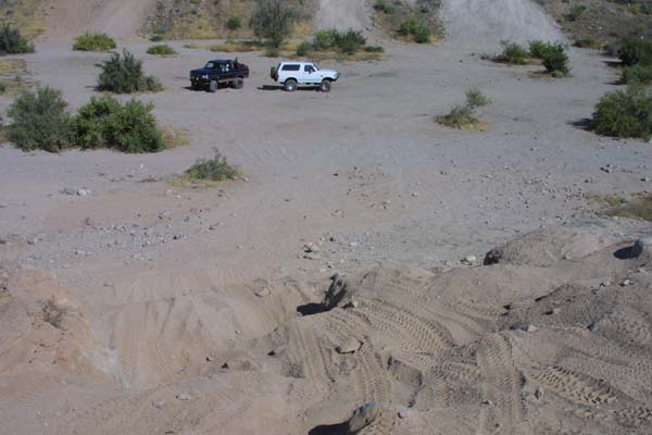 White and dark 4x4 SUVs parked in a sandy desert wash covered in tire tracks