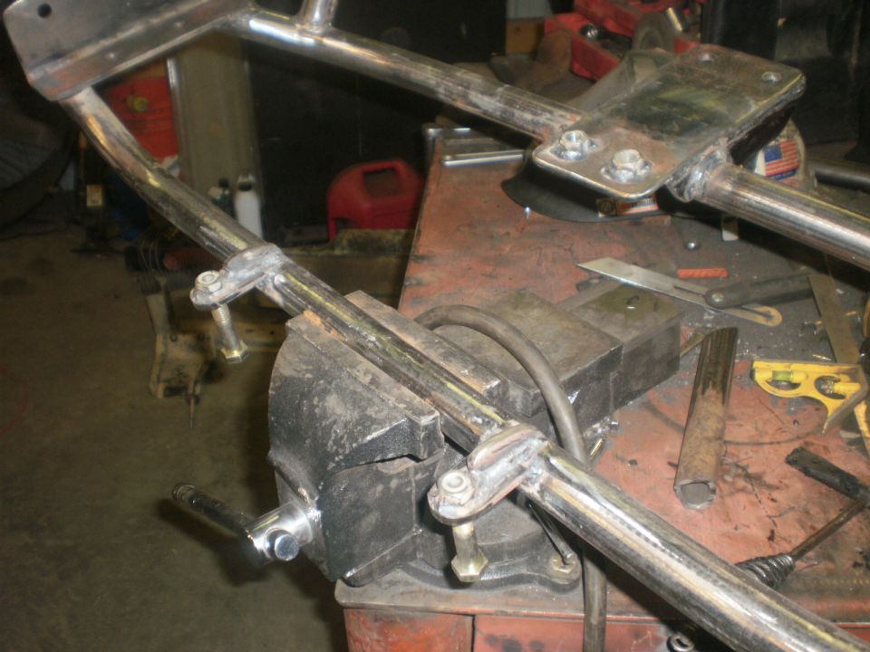 Metal frame assembly clamped in a vise on a workbench, with tools scattered around
