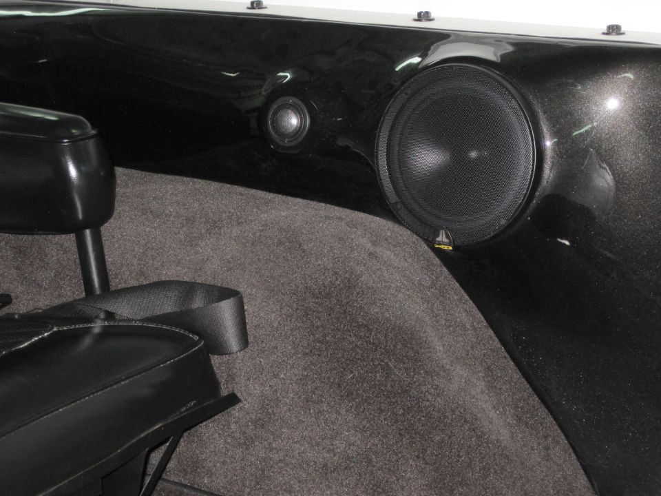JL Audio speaker and tweeter in black metal-flake fiberglass panel with gray carpet, black seat in foreground
