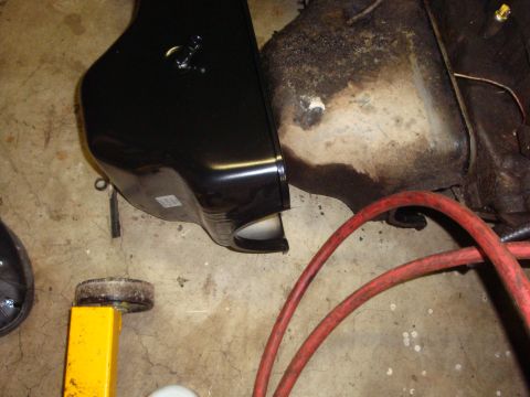 1989 Ford Bronco - Close-up of a black fuel tank and a greasy engine part, with red hoses visible on the floor.