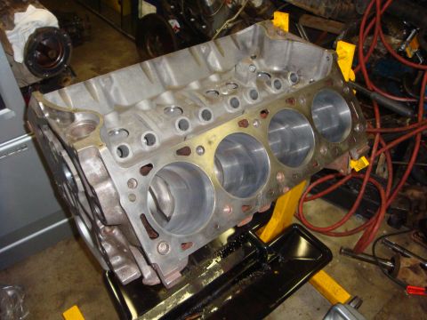 1989 Ford Bronco - A bare engine block is supported by a yellow stand in a workshop setting, ready for assembly.