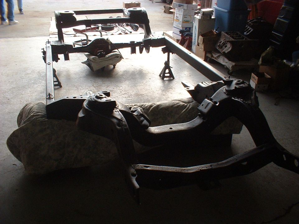 Car frame assembly with rear axle and suspension components, resting on jack stands and padding