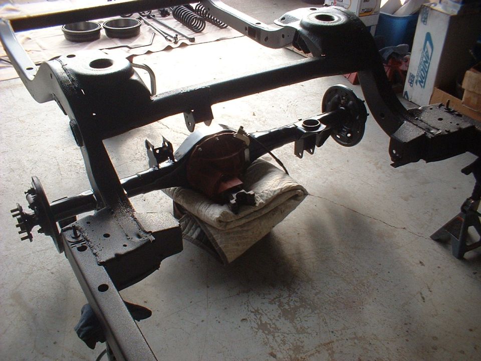 Car frame and rear axle assembly on jack stands, possibly undergoing restoration