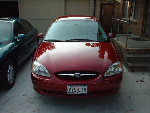 1996 Ford Taurus - A red Ford sedan is parked in front of a garage, with another car to its left.