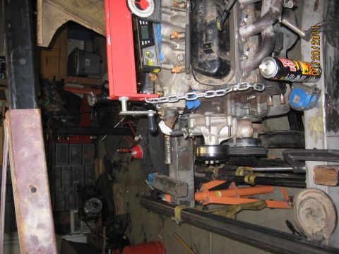 1961 International Scout 800 - Engine and transmission assembly supported by a red engine hoist in a cluttered garage environment.