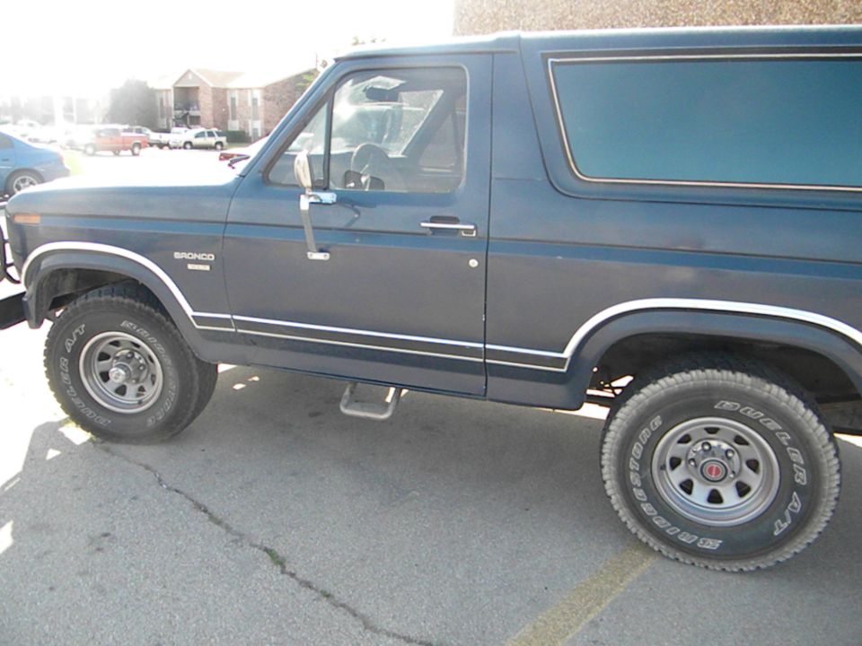 Dark blue Ford Bronco side view, showing the front fender, door, rear quarter panel, and wheels. A step bar is visible below the door