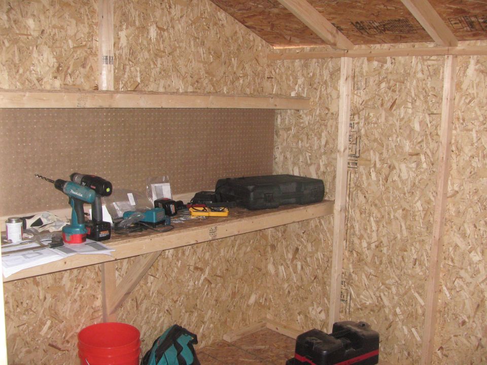 Interior of a shed with shelves holding drills, batteries, and a toolbox