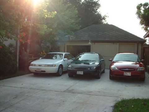 1996 Ford Taurus - Three Ford Taurus sedans are parked in a driveway in front of a garage.