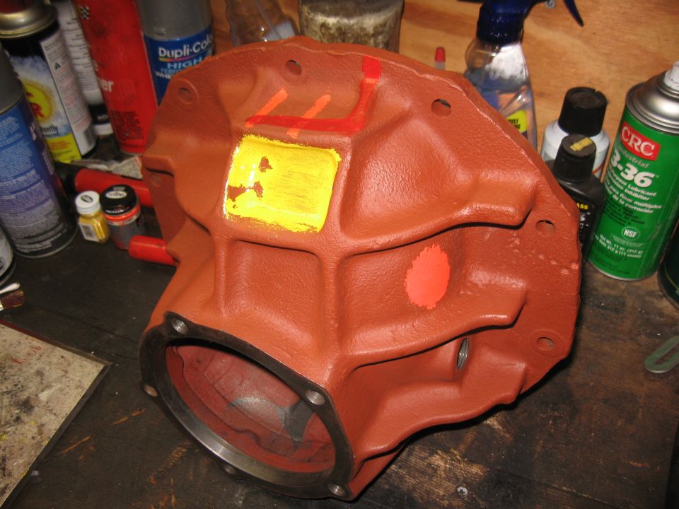 Differential housing with yellow and red markings on a workbench with spray cans