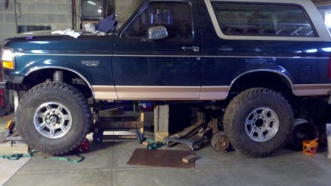 1995 Ford Bronco - A dark green 1995 Ford Bronco with tan trim is shown with its suspension lifted and resting on blocks.