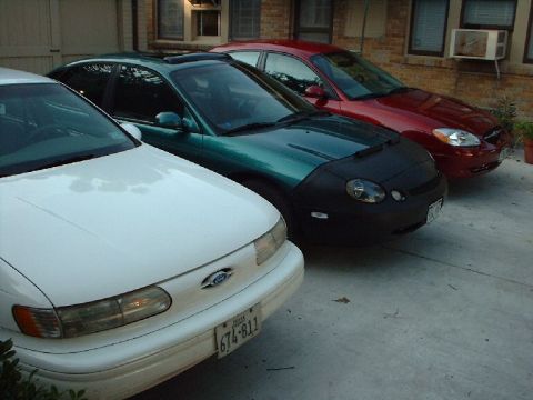 1996 Ford Taurus - Three cars are parked in a row, including a white 1996 Ford Taurus in the foreground.