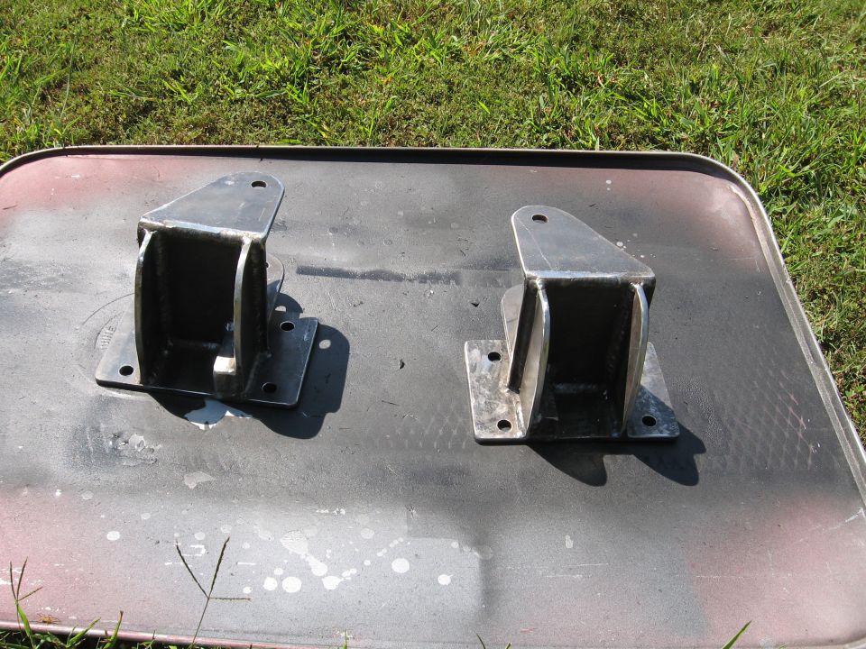 Two welded steel suspension mounting brackets on a black mat over grass