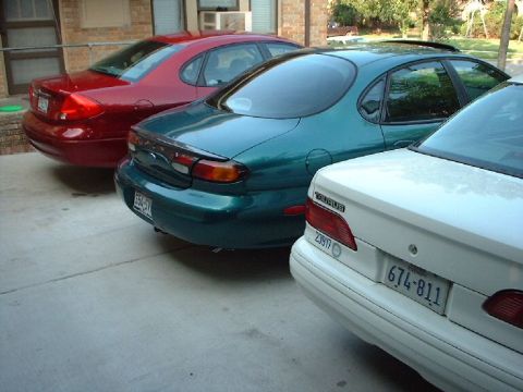 1996 Ford Taurus - Three sedans, including a teal Ford Taurus, are parked in a lot.