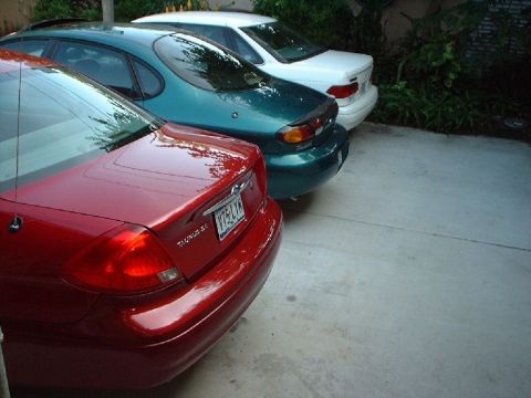 1996 Ford Taurus - Three sedans are parked in a concrete driveway, showing their rear ends.