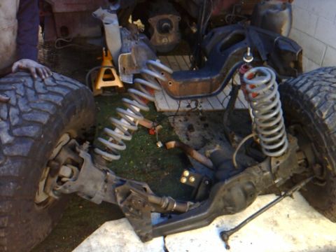 1989 Ford Bronco - The front suspension and large tire of a vehicle are visible, suggesting it is undergoing repair or modification. A watermark for SUPERMOTO…