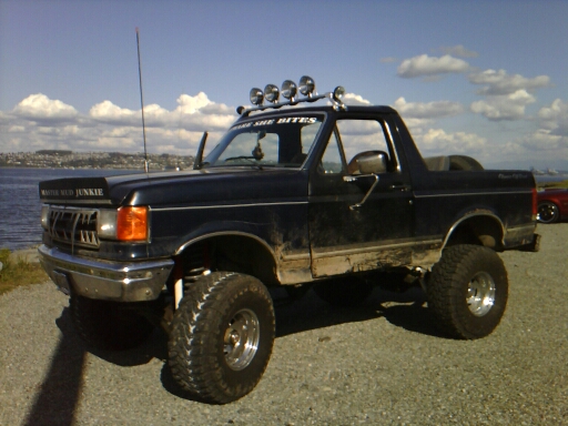 Black lifted Ford pickup with light bar by the water
