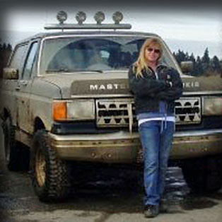 1989 Ford Bronco - A woman stands in front of a dusty Ford Bronco with a custom grille and roof-mounted lights.