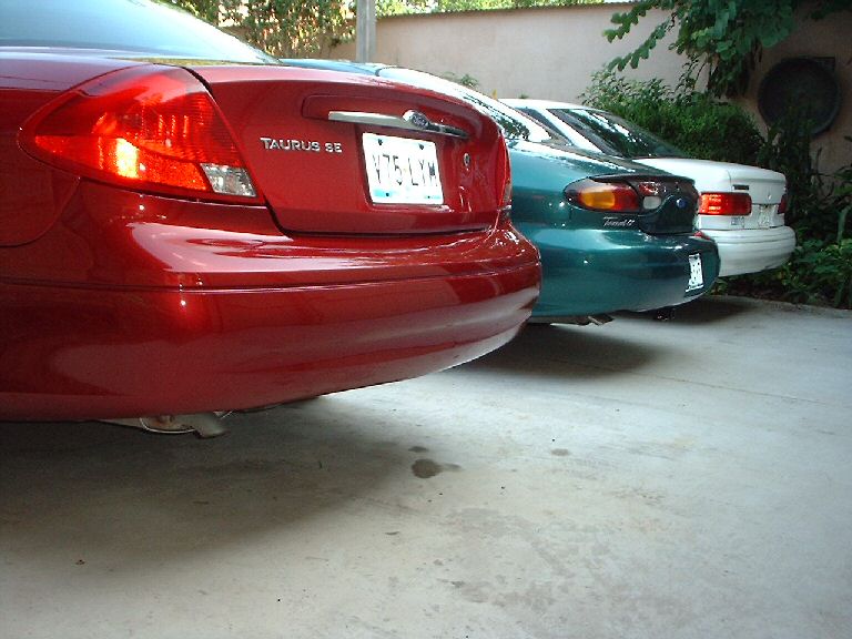 Red 1996 Ford Taurus SE rear view, license plate V75 LYM, parked next to green and white cars