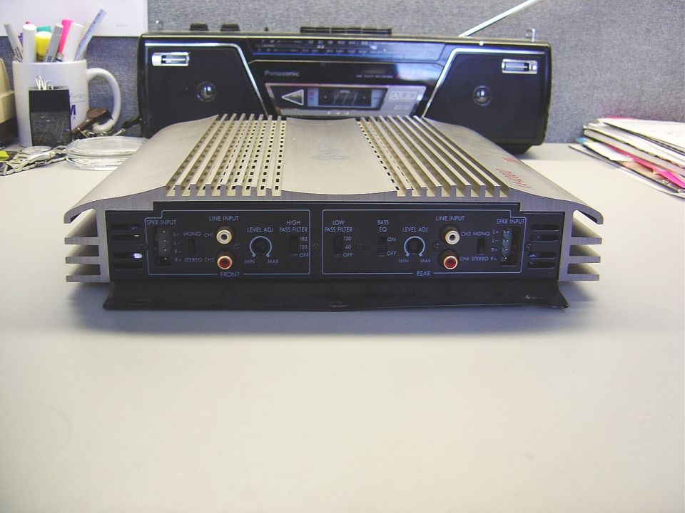Car audio amplifier with silver fins and black faceplate, next to a black boombox