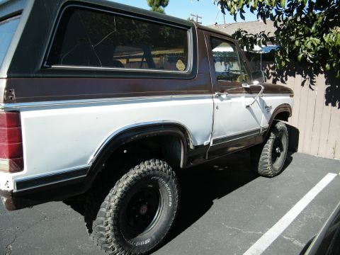 1982 Ford Bronco - This two-tone Ford Bronco is parked outside on a sunny day, showing its off-road tires and a damaged rear window.